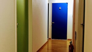A hallway with wooden flooring, green and blue doors, and a fire extinguisher on the right. - Guesthouse LuLuLu (Kochi)