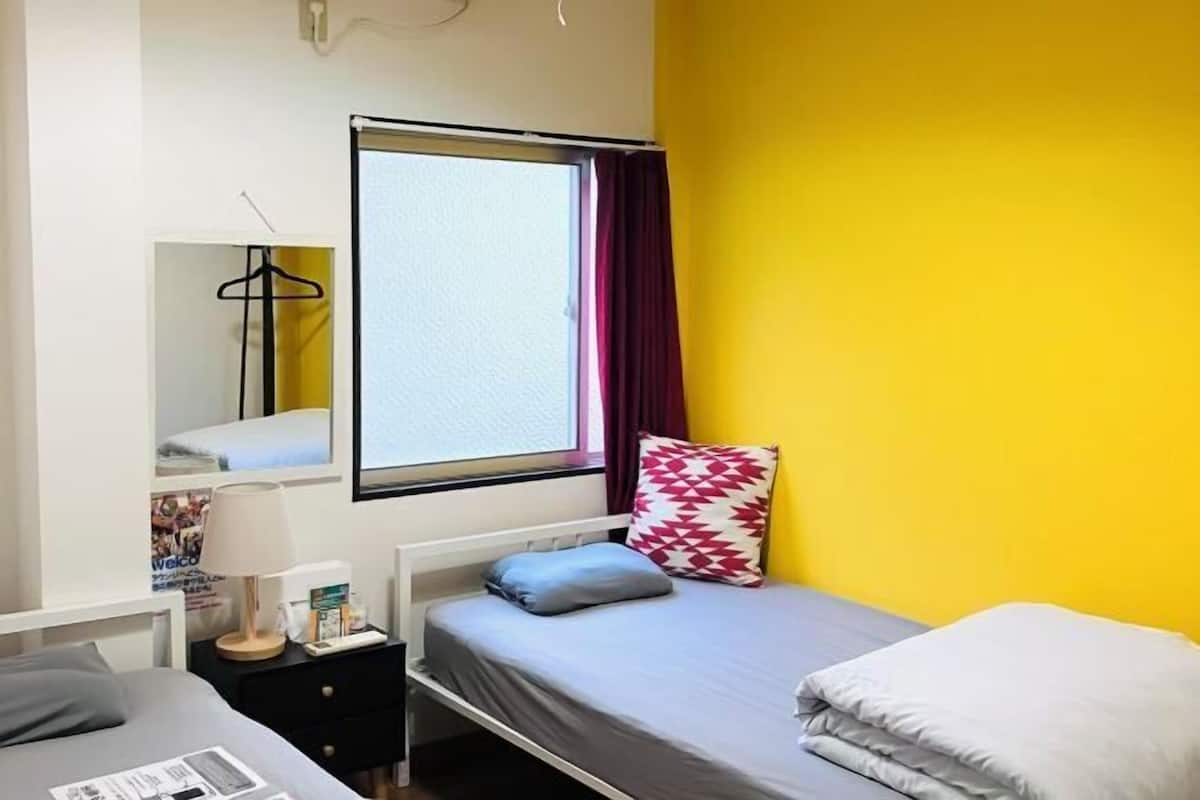 A bedroom with a bed, a bedside table, a window with curtains, and a mirror on the wall.