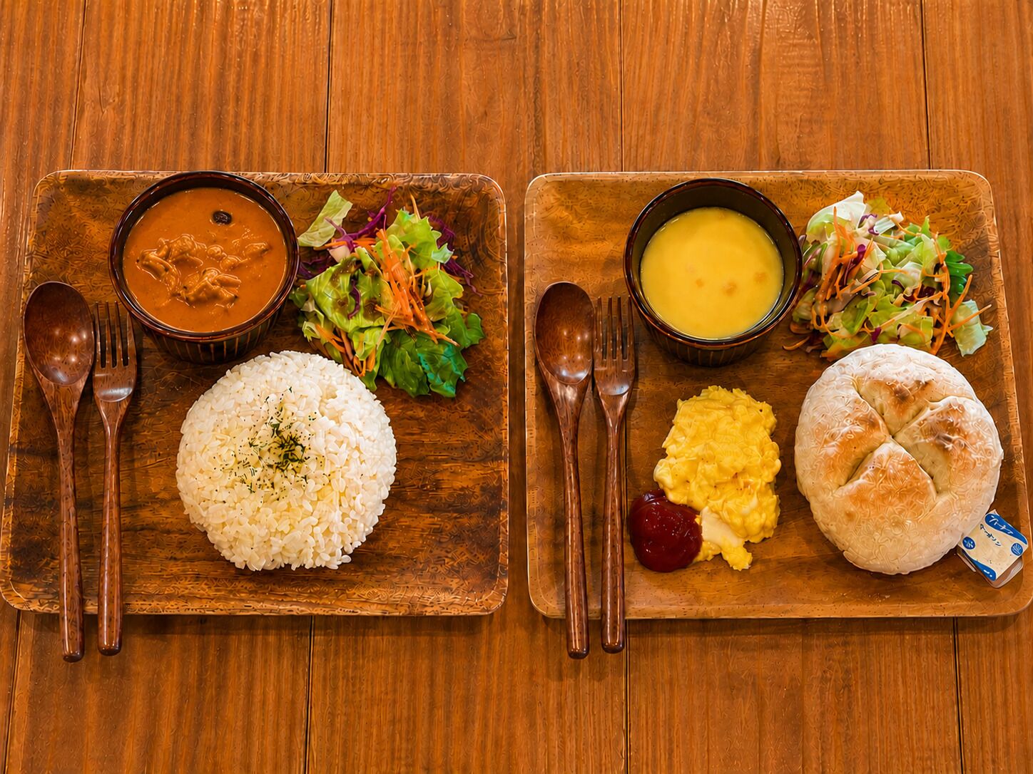 Two wooden serving platters with food items, utensils, and a wooden table.