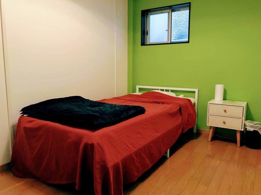 A bedroom with a bed, a nightstand, and a window.