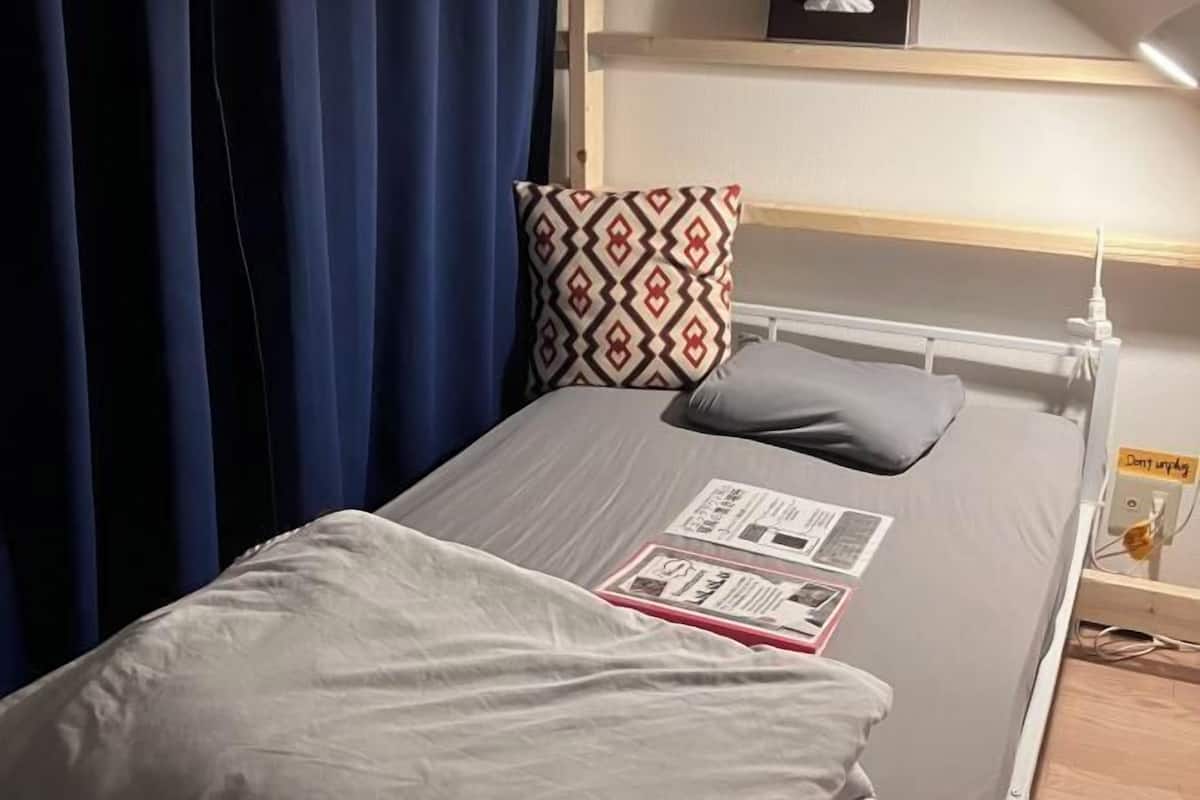A single bed with a grey blanket, a patterned pillow, and a bedside table with a lamp.
