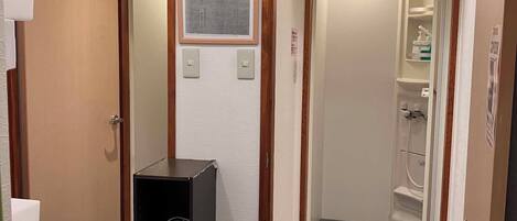Un baño pequeño con lavamanos, un cubo de basura, zona de ducha y un reloj en la pared.