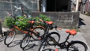 A bicycle parked in front of a building with a chain-link fence and a concrete wall. - Guesthouse LuLuLu (Kochi)