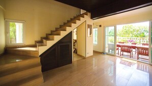Una habitación amplia con una escalera de madera, un cerramiento de vidrio corredera que da a un espacio exterior con patio y mobiliario.