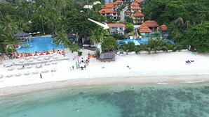 Un resort con varias piscinas, una playa y bungalows sobre el agua.