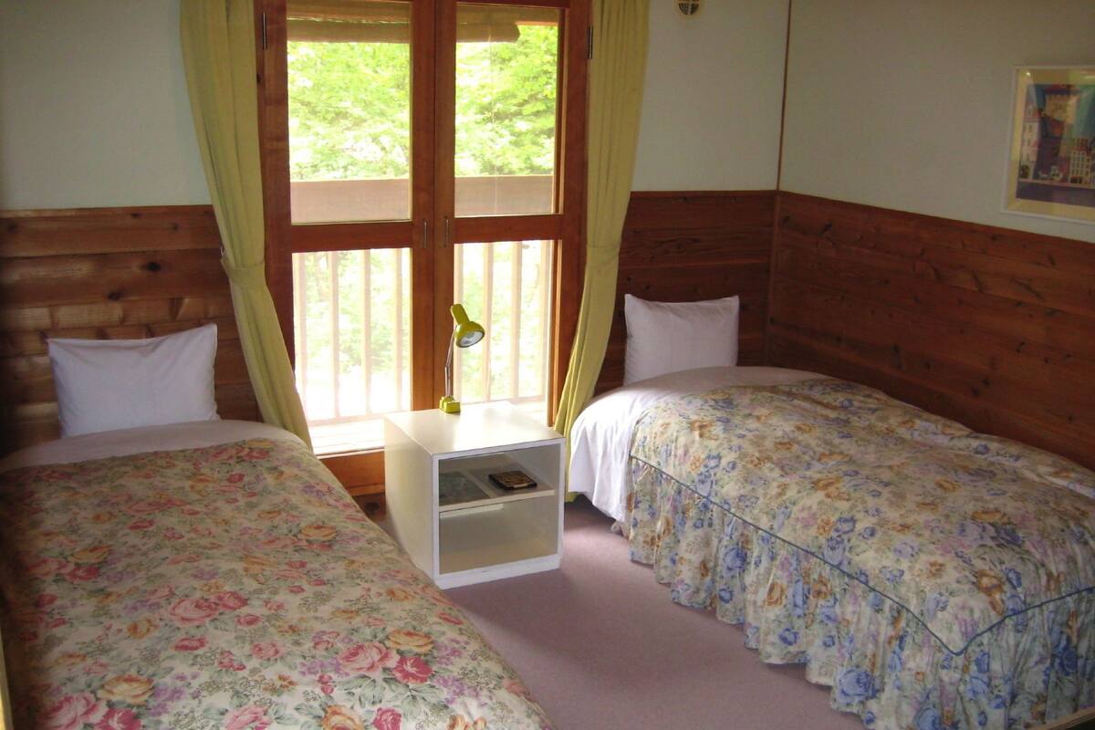 Une chambre avec deux lits, des têtes de lit en bois, une table de chevet avec une lampe et une fenêtre avec des rideaux.