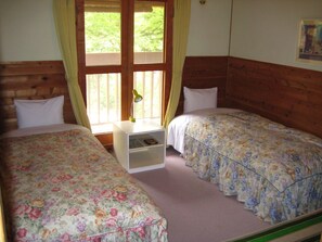 A bedroom with two beds, wooden headboards, a nightstand with a lamp, and a window with curtains.