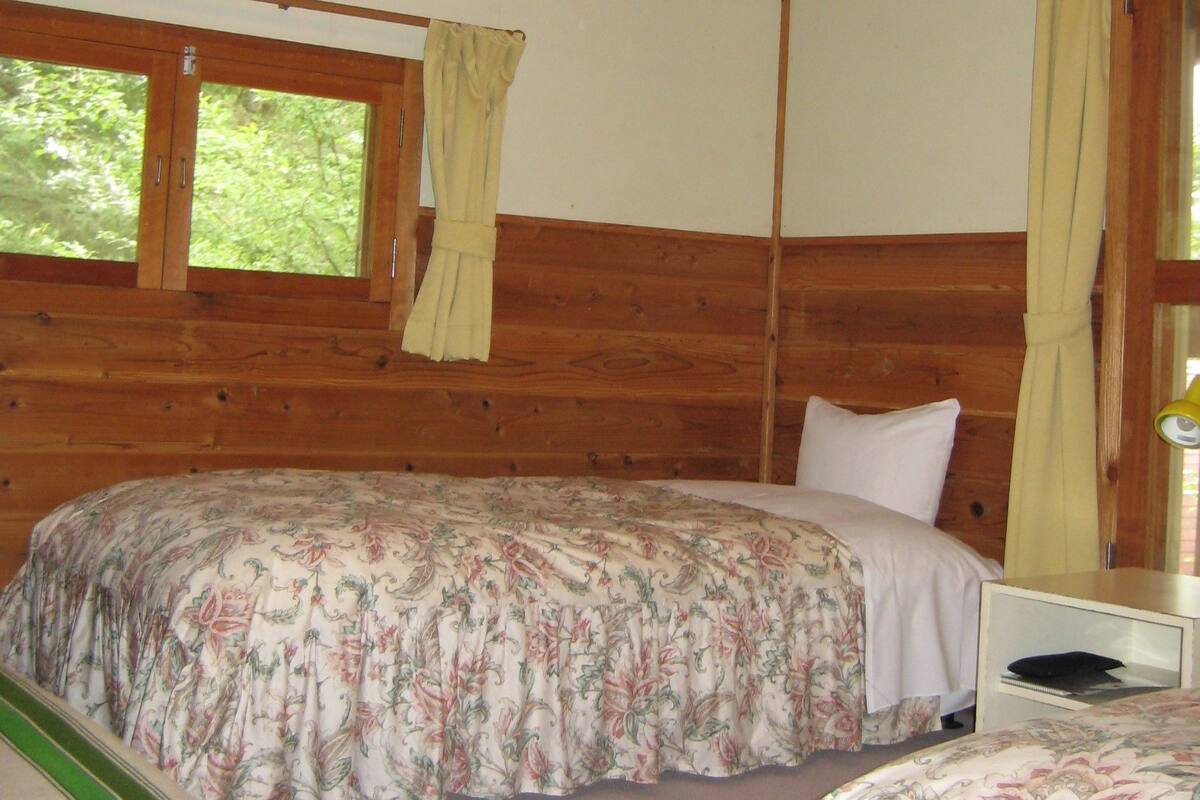 Une chambre dans un chalet en bois, avec deux lits, une fenêtre avec des rideaux et un plafond en bois.
