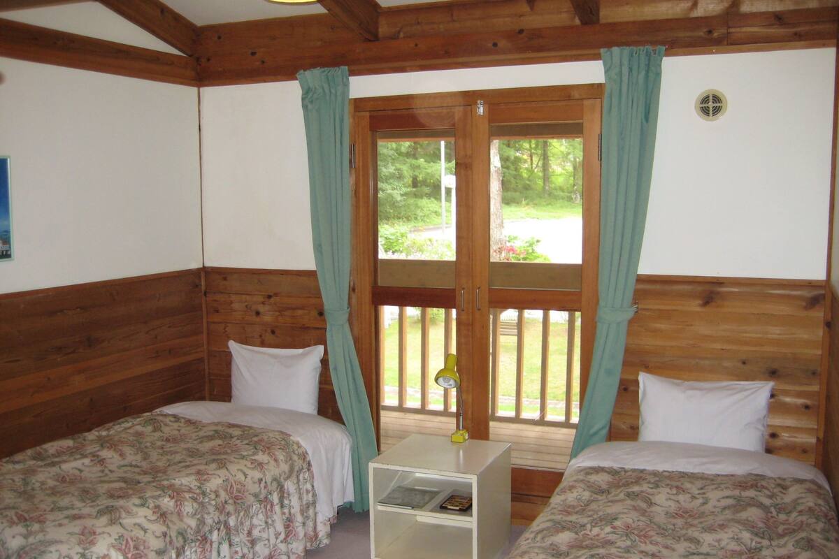 Une chambre avec deux lits, des murs en bois, une fenêtre avec des rideaux et une petite table avec une lampe.