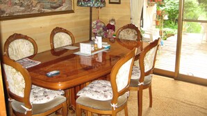 A dining room with a wooden table, six chairs, a painting, a clock, and a window with a view of greenery. - Hirotani Pension & Lodge (Hara)