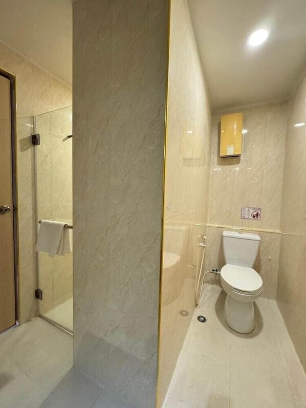 A bathroom with a toilet, a glass-enclosed shower, and a towel rack. - Jolly Suites & Spa Thaphra (Bangkok)
