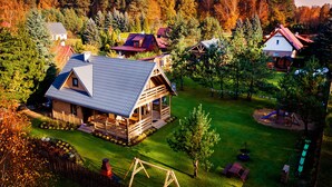 A wooden cabin with a sloped roof, surrounded by a well-maintained lawn and trees. - Winiec Family Houses (Winiec)