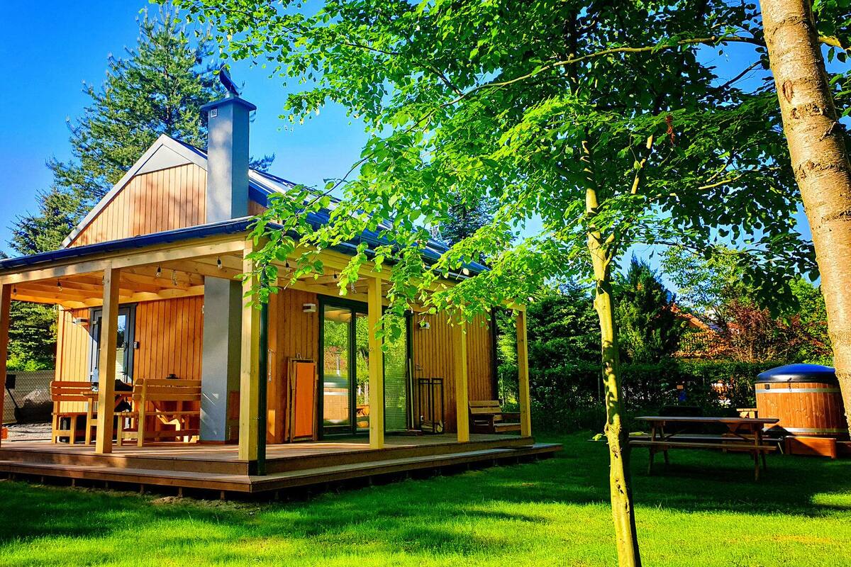Une cabane en bois dotée d’un porche, d’une cheminée et d’un espace extérieur abrité avec des sièges.