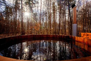A circular wooden deck with a reflective water surface, surrounded by tall trees and a wooden structure with a cylindrical object on top. - Winiec Family Houses (Winiec)
