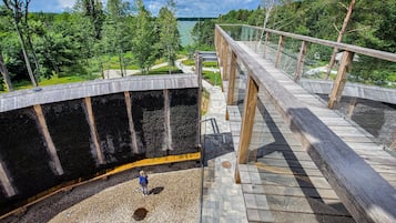 A wooden deck with glass railings overlooking a lake, surrounded by trees.