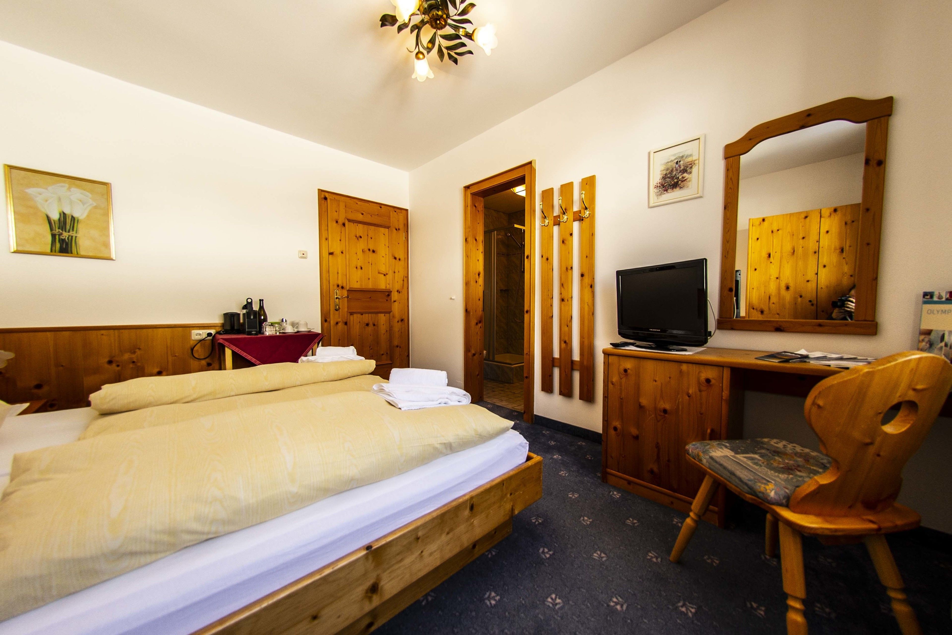 A hotel room with a wooden bed, a desk with a television, a chair, and a mirror.
