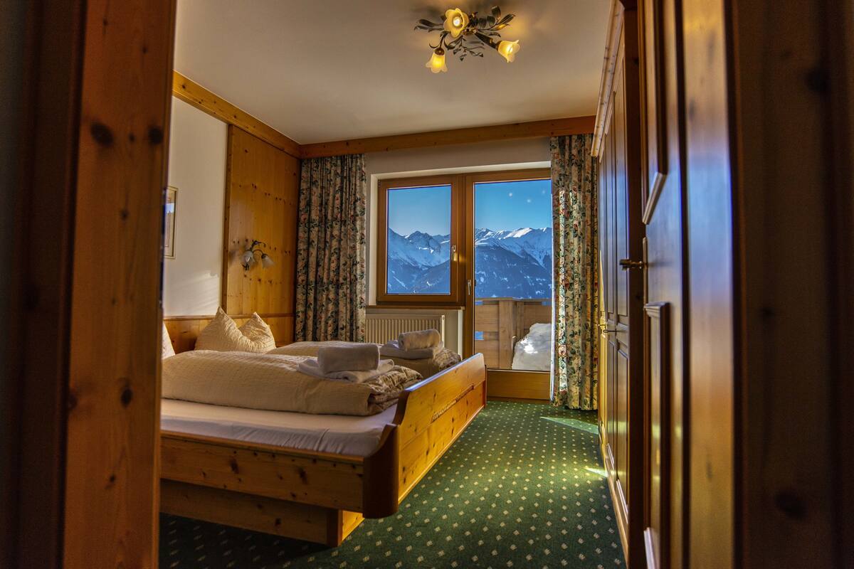 A wooden bedroom with a bed, a window with a mountain view, and a wooden wardrobe.