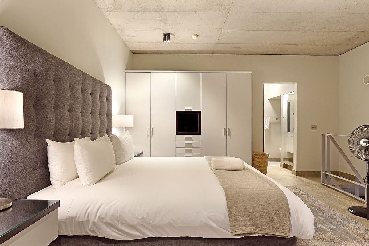 A hotel room with a large bed, a flat-screen TV, a bedside table, and a fan.
