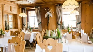 Um restaurante acolhedor com paredes e mesas de madeira preparadas para refeições, com recortes em formato de coração nas cadeiras e um ambiente quente e convidativo.