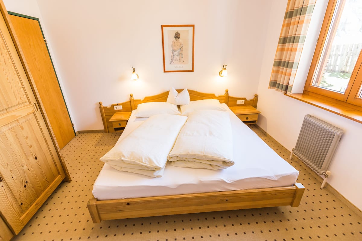 Ein ordentlich bezogenes Bett mit weißen Leinentüchern, einem hölzernen Kopfteil und zwei Nachttischlampen.
