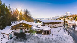 Estância de montanha coberta de neve, com edifícios, incluindo um restaurante chamado 'Dorfkrug', e vista para montanhas nevadas ao fundo.