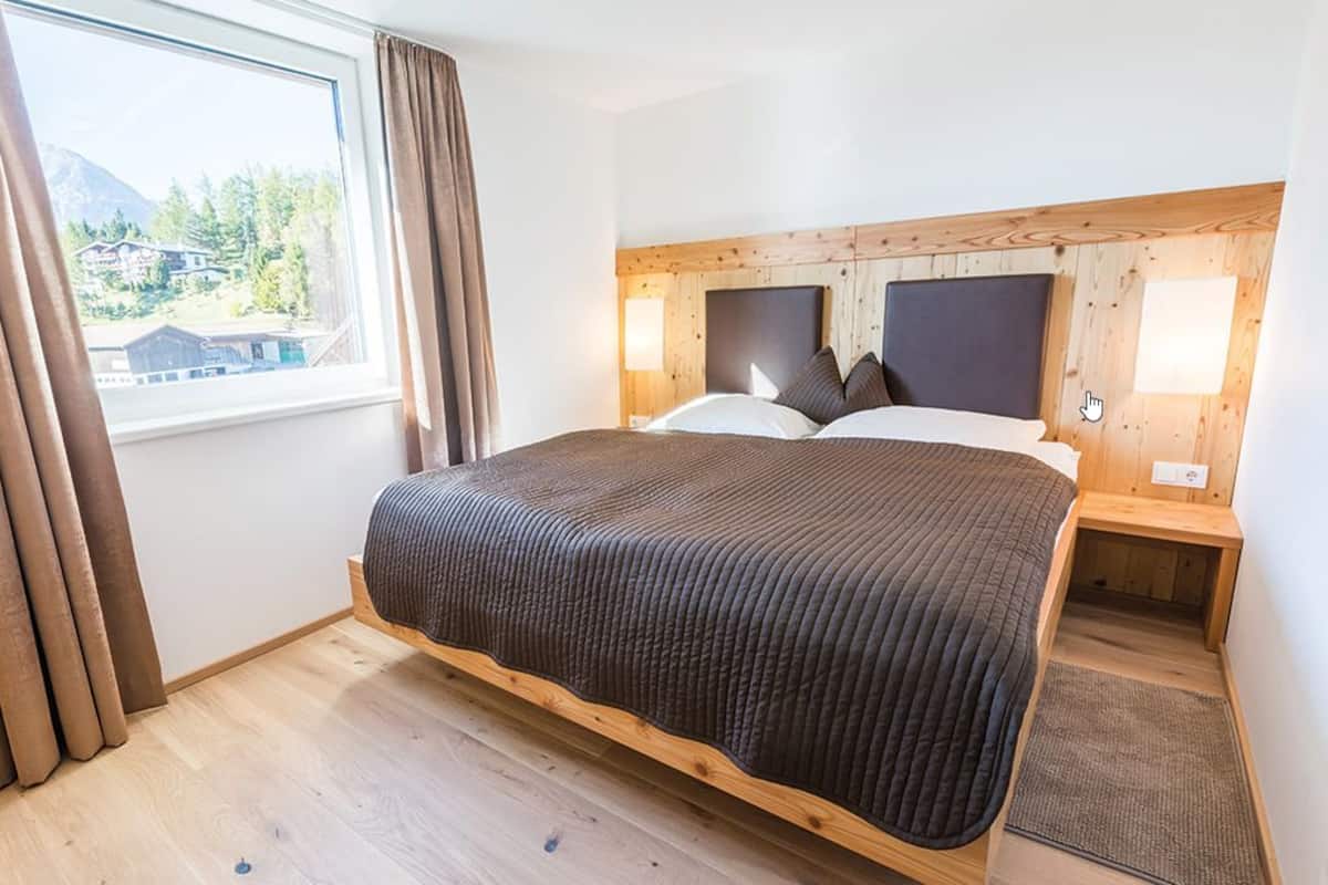 Ein Schlafzimmer mit einem großen Bett, einem Holzkopfteil, Nachttischlampen und Blick auf einen Berg durch ein Fenster.