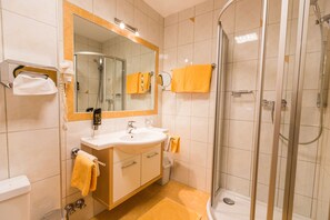 Un baño moderno con ducha de vidrio, un lavamanos con espejo y un inodoro.