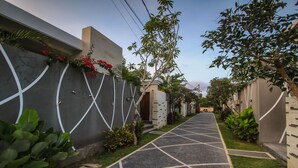 A narrow, paved pathway flanked by walls with geometric white designs and lush greenery. - Giri Ungasan Villa (Ungasan)