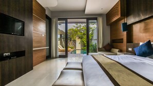 A modern hotel room with a large bed, a TV mounted on the wall, and a sliding glass door leading to an outdoor area with a pool and lounge chairs. - Giri Ungasan Villa (Ungasan)