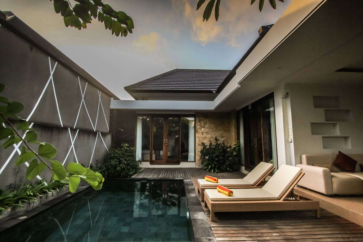 Un área de piscina moderna al aire libre con sillones de descanso y una terraza de madera.