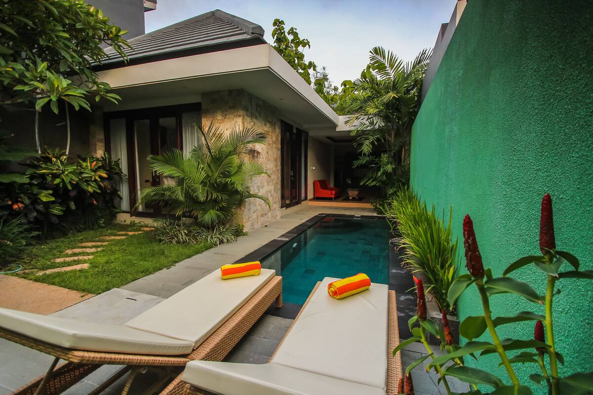 Una casa moderna con piscina, sillas de descanso y un muro cubierto de plantas.