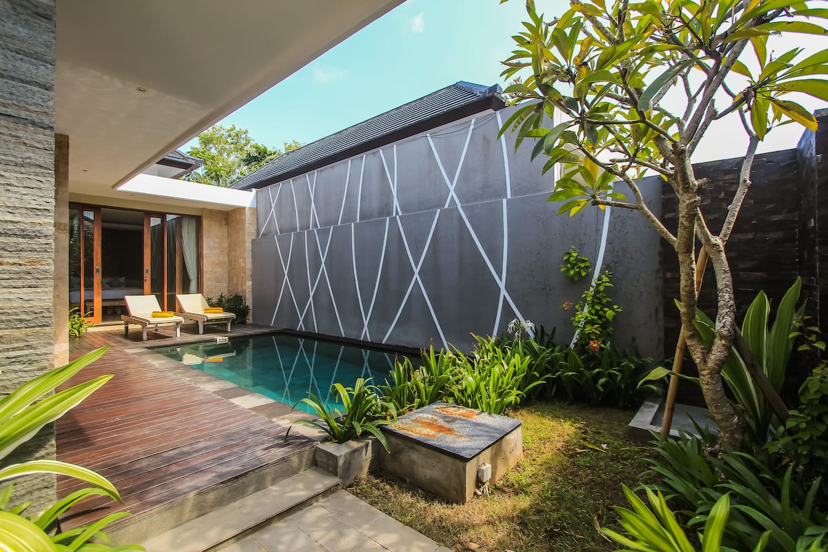 Un área de piscina moderna al aire libre con una terraza de madera, sillones de descanso y un diseño de pared geométrico.