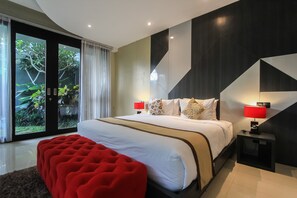 Een moderne slaapkamer met een groot bed, twee nachtkastjes met lampen, een rode poef en een schuifdeur van glas naar een tuin.