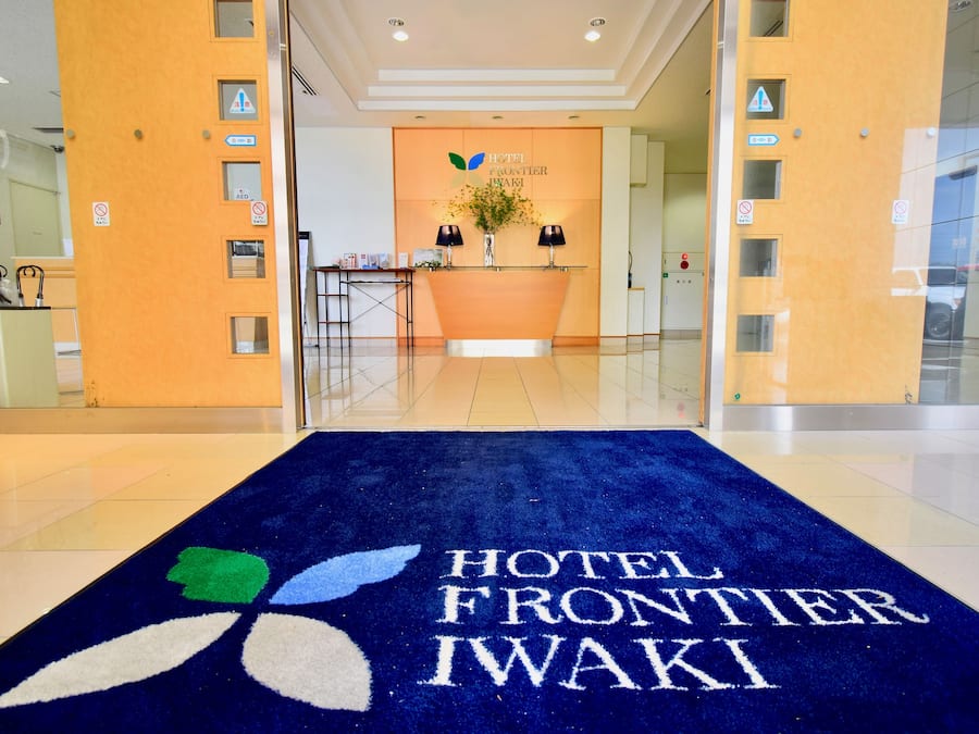 Zona de recepción de un hotel con alfombra azul que muestra el nombre del hotel, un mostrador de recepción y un cartel en la pared.
