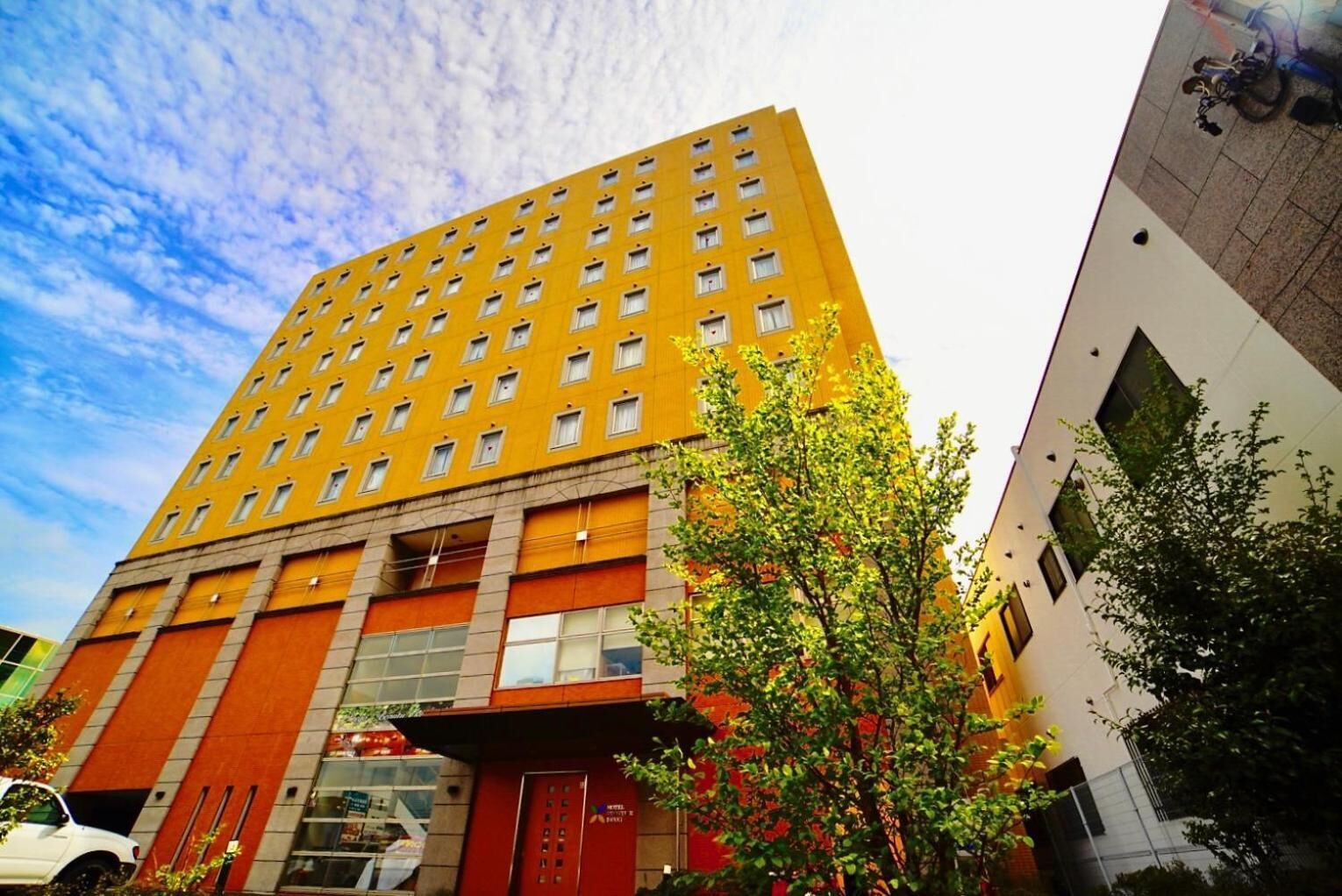 Un hôtel à plusieurs étages, avec une façade jaune, de grandes fenêtres et une entrée rouge.