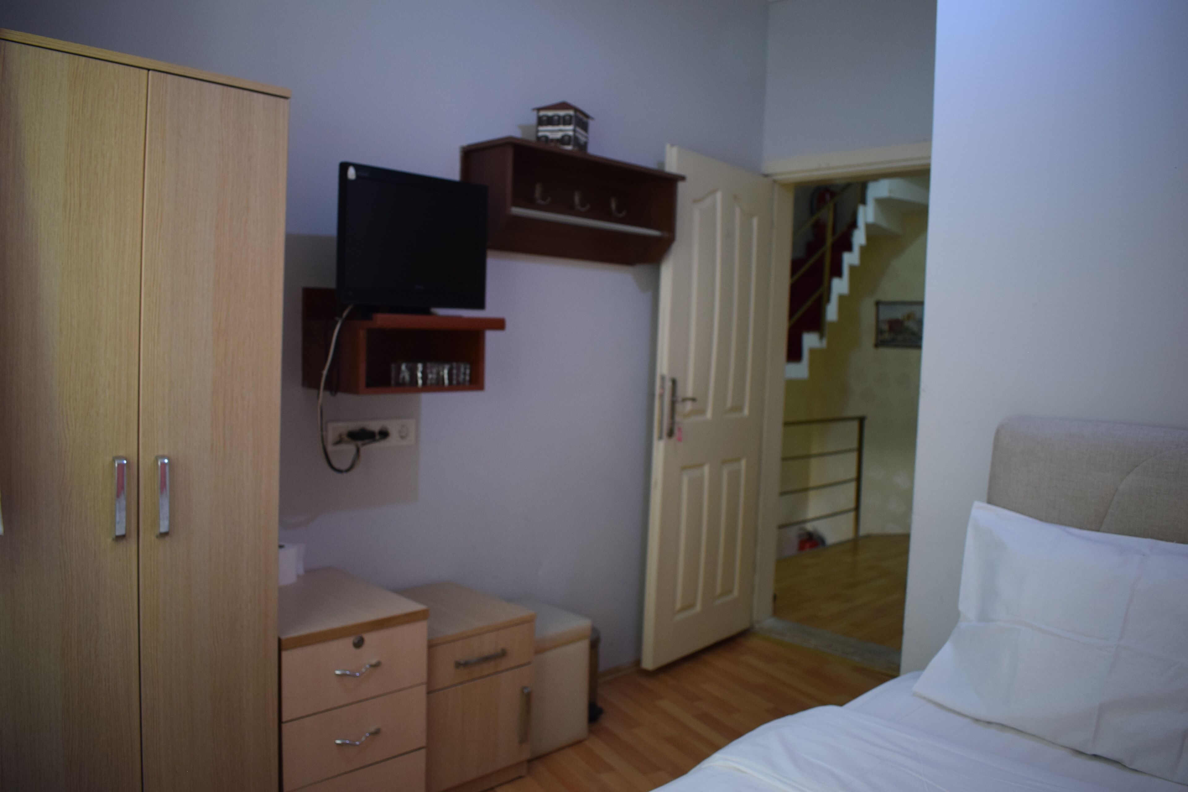 Une chambre à coucher comprenant un lit, une armoire, un bureau, un téléviseur et une porte donnant sur un escalier.
