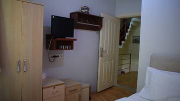 Une chambre à coucher comprenant un lit, une armoire, un bureau, un téléviseur et une porte donnant sur un escalier.