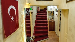 Un escalier recouvert d’une moquette rouge mène à un palier où se trouve un tableau encadré et une petite table sur laquelle est posé un vase de fleurs.