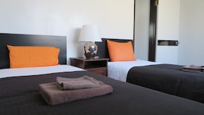 A hotel room with two beds, each with an orange pillow and a dark-colored bedspread. There is a nightstand with a lamp between the beds. - Spacious Apartment - 5-7 minute walk to Shinkansen and Shin-Kobe Subway Station (Kobe)