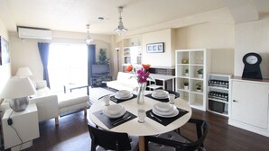A dining area with a round table set for four, white walls, a ceiling fan, and a window with curtains. - Spacious Apartment - 5-7 minute walk to Shinkansen and Shin-Kobe Subway Station (Kobe)