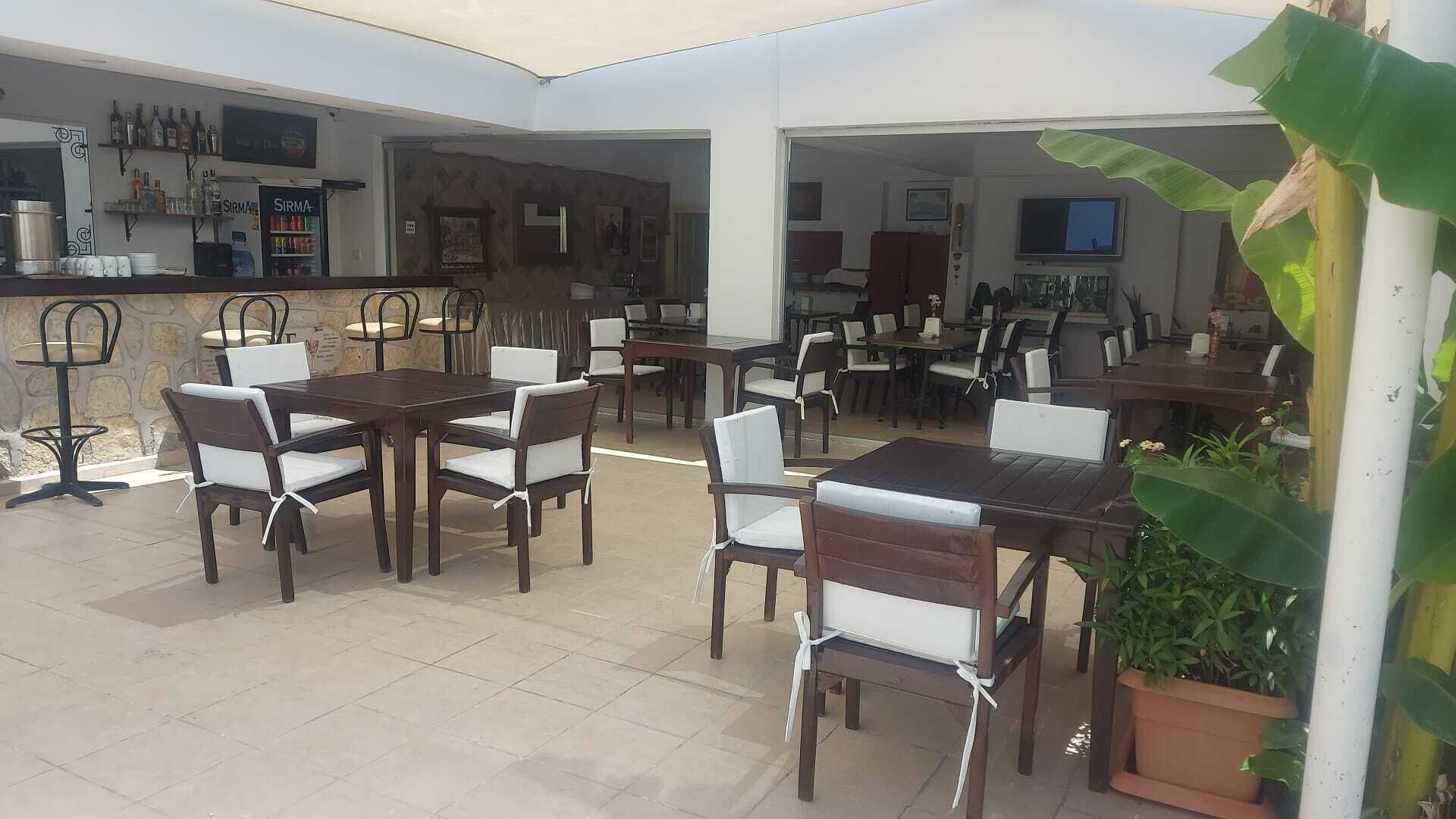 Ein Außenbereich mit einer Terrasse, mehreren Esstischen und Stühlen, einer Bar mit Flaschenregalen und einem an der Wand befestigten Fernseher.