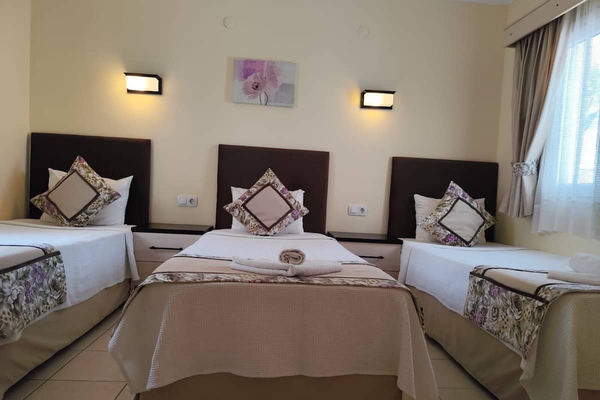 Une chambre d’hôtel avec trois lits, chacun doté d’une tête de lit et de coussins décoratifs, un grand lit au centre et deux appliques murales.