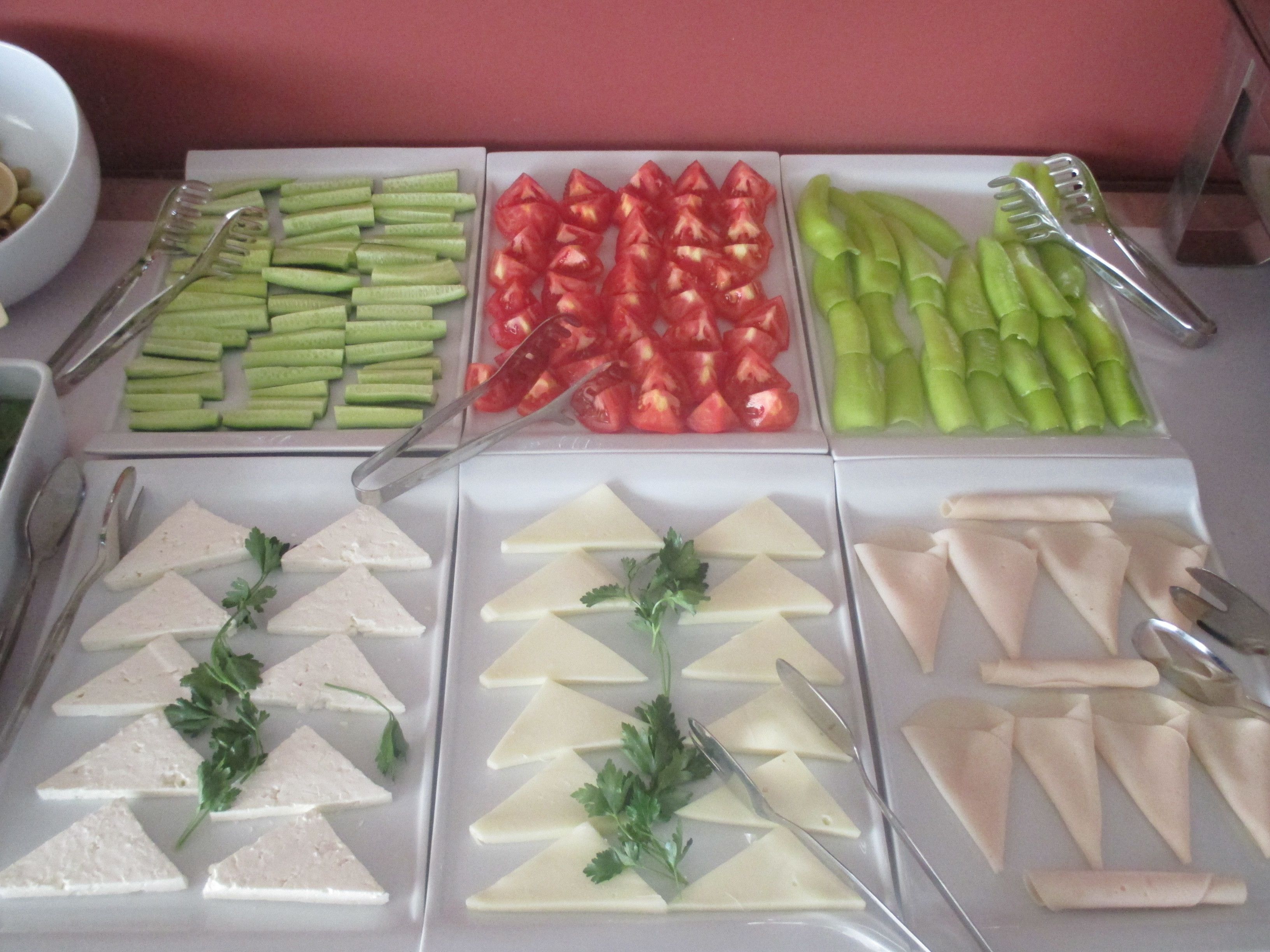 Un bufé con diversos alimentos, incluyendo verduras, queso y carne, dispuestos en bandejas.