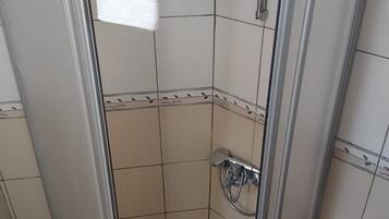 Un box de ducha con puerta de cristal, una toalla colgada en la puerta y un secamanos en la pared.