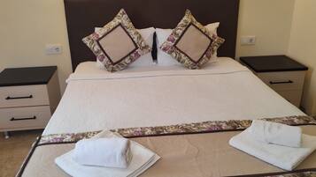 A neatly made bed with floral-patterned pillows and a matching headboard, flanked by bedside tables with lamps, in a well-lit room.