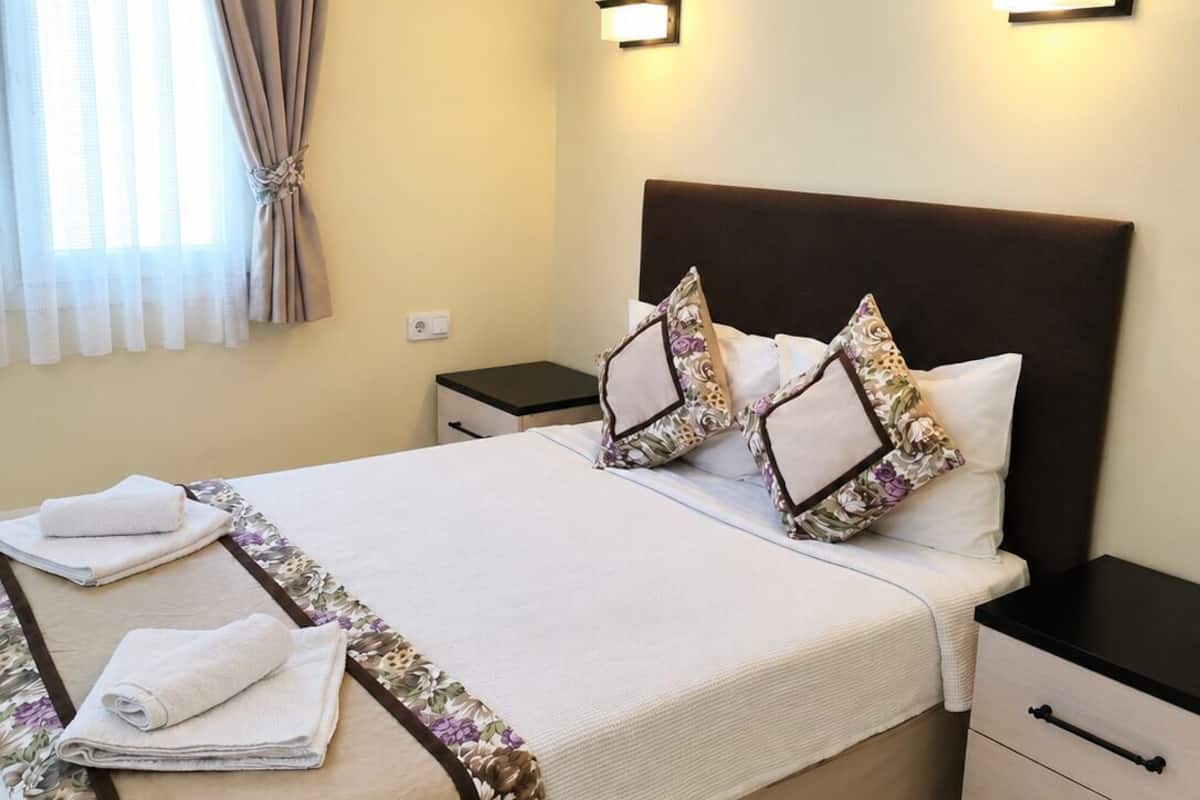 Une chambre d’hôtel avec un lit, des tables de chevet, une commode et une fenêtre avec des rideaux.
