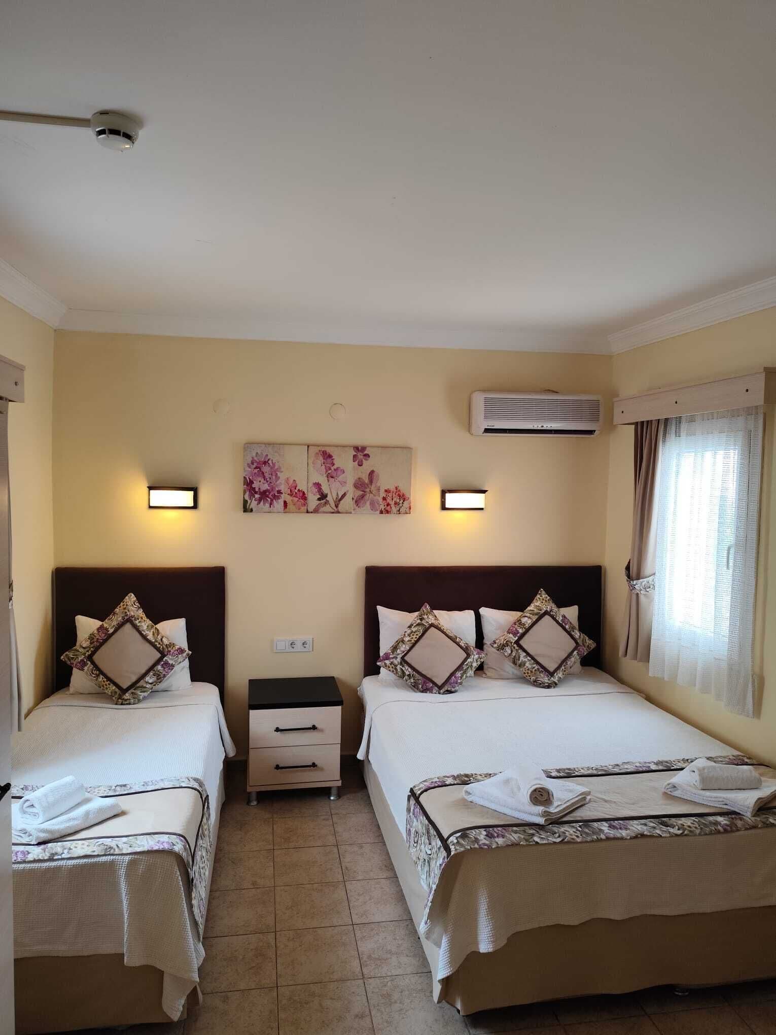 Une chambre d’hôtel avec deux lits, une table de chevet, un climatiseur fixé au mur et une fenêtre avec des rideaux.
