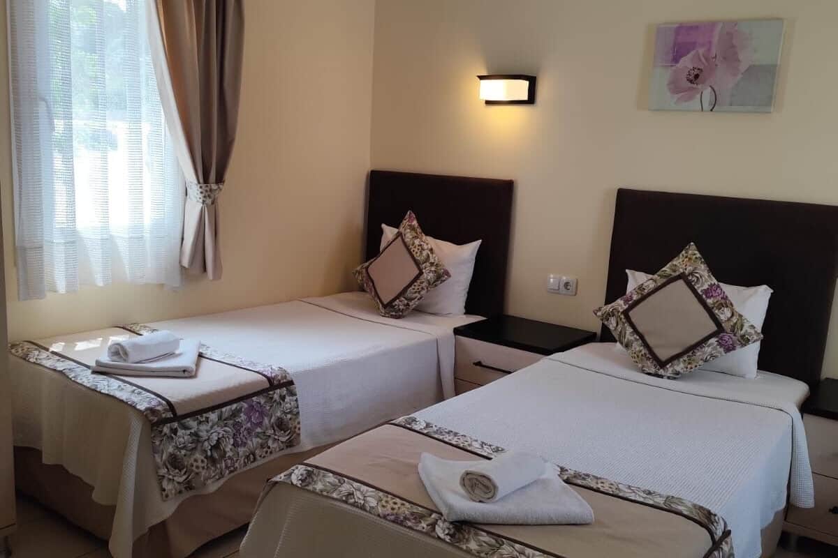 Une chambre d’hôtel avec deux lits, une table de chevet, une lampe fixée au mur et une fenêtre avec des rideaux.