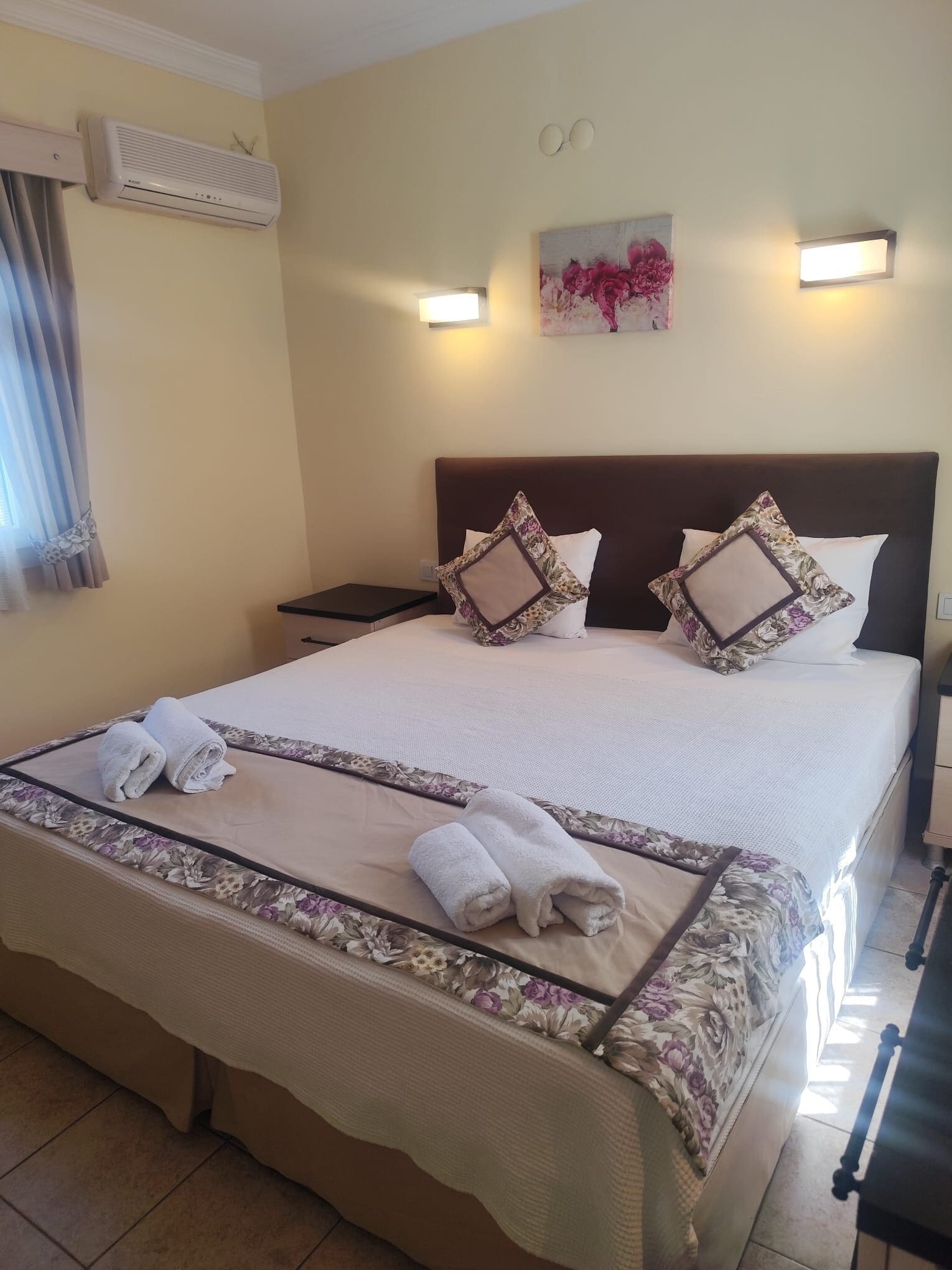 A neatly made bed with floral bedding, a headboard, and two bedside tables.
