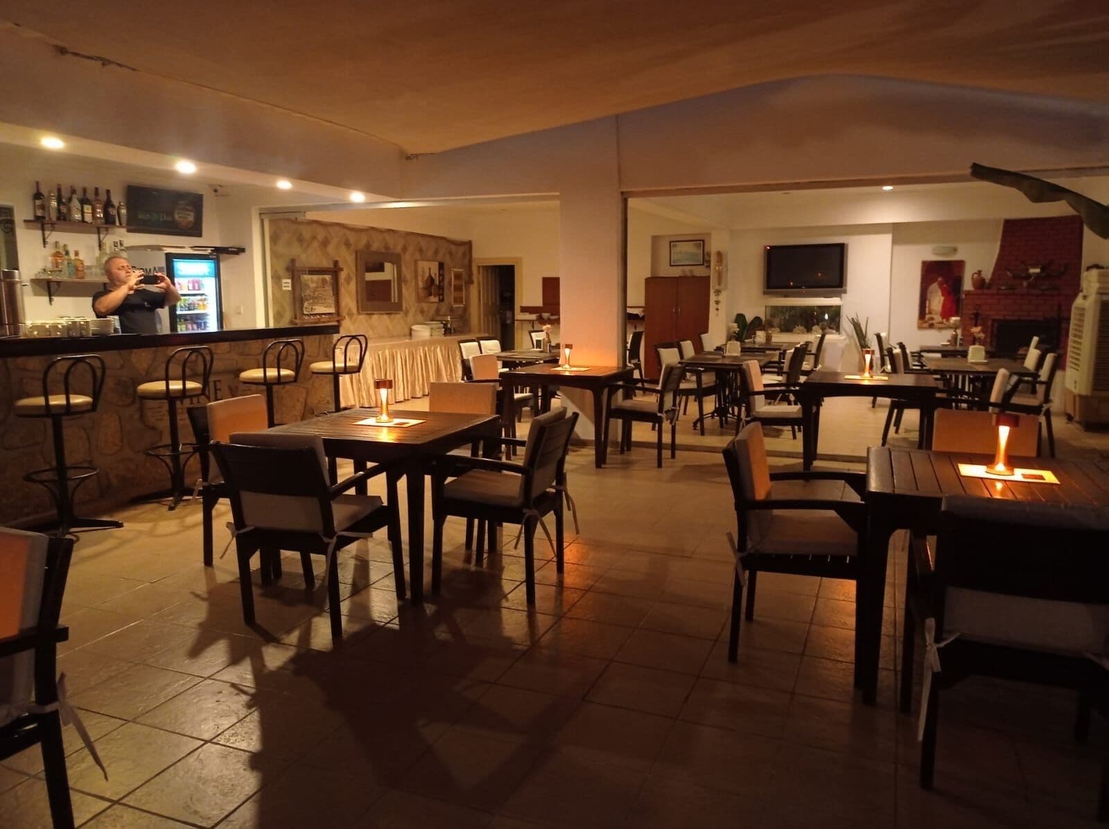 Un restaurante con barra, varias mesas y sillas, y una chimenea al fondo.